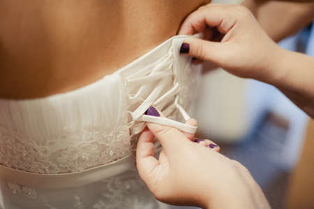 Fashionable bridesmaids dresses helped wear bow on back of wedding dress bride. Morning wedding day.の写真素材