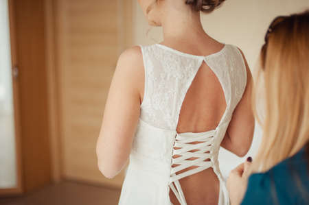Fashionable bridesmaids dresses helped wear bow on back of wedding dress bride. Morning wedding day.の写真素材