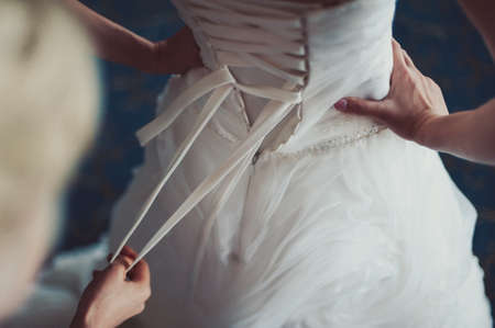 Fashionable bridesmaids dresses helped wear bow on back of wedding dress bride. Morning wedding day.の写真素材