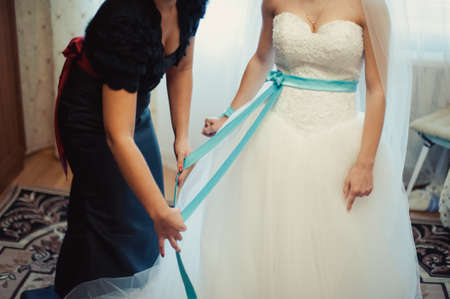Fashionable bridesmaids dresses helped wear bow on back of wedding dress bride. Morning wedding day.の写真素材