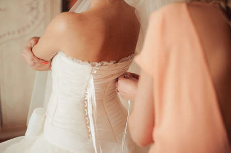 Fashionable bridesmaids dresses helped wear bow on back of wedding dress bride. Morning wedding day.の写真素材