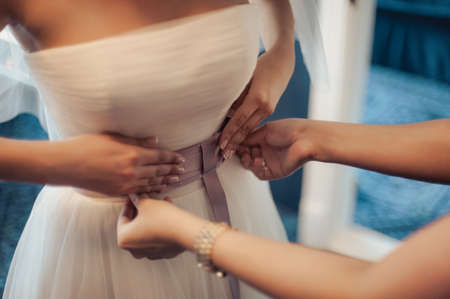 Fashionable bridesmaids dresses helped wear bow on back of wedding dress bride. Morning wedding day.の写真素材