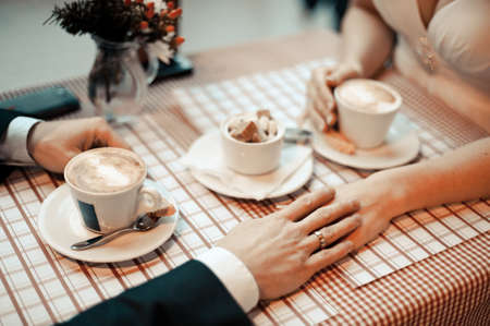 Couple drinks coffee. Closeup view of married couple holding handsの写真素材