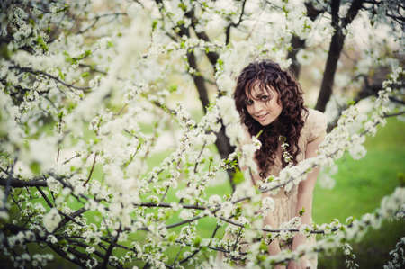 A curly brunette girl standing in blossoming trees