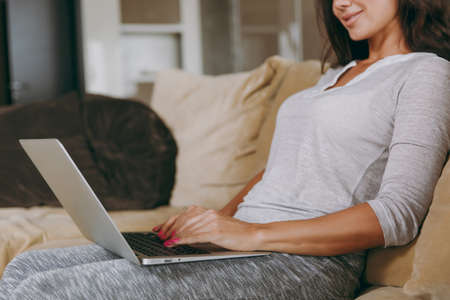 The beautiful young woman at home sitting on the sofa, relaxing in her living room and working with laptop. Close up.の写真素材