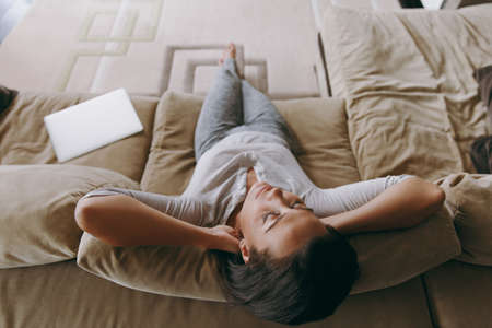 The young woman at home lying on the sofa and relaxing in her living room with her hands under her head. Close up. View from above.の写真素材