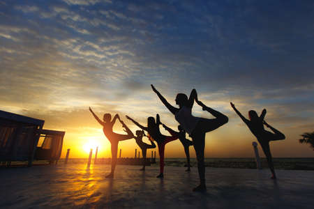 The group of women doing yoga at sunrise near the seaの写真素材
