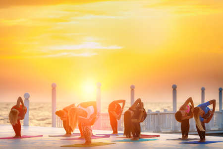 The group of women doing yoga at sunrise near the seaの写真素材