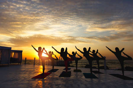 The group of women doing yoga at sunrise near the seaの写真素材