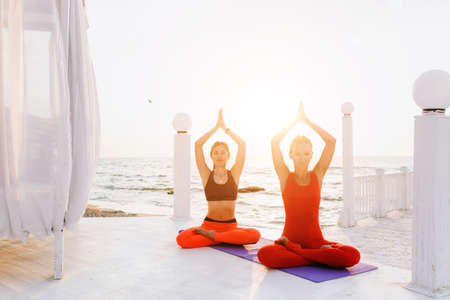 A two women do yoga at sunrise near the seaの写真素材