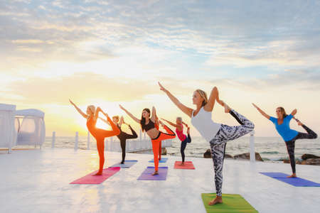 The group of women doing yoga at sunrise near the seaの写真素材