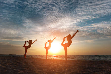 The group of women doing yoga at sunrise near the seaの写真素材