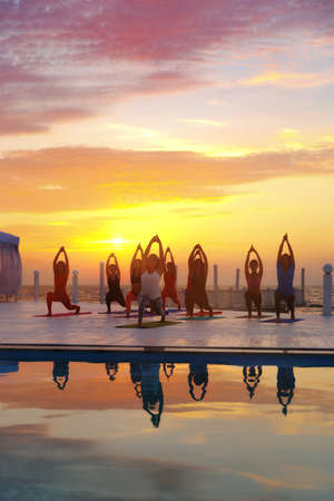 The group of women doing yoga at sunrise near the seaの写真素材