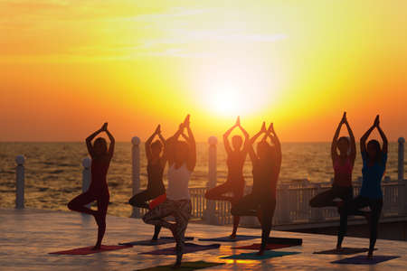 The group of women doing yoga at sunrise near the seaの写真素材