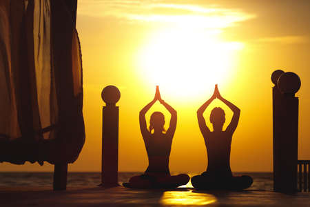 A two women do yoga at sunrise near the seaの写真素材
