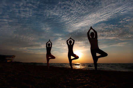 The group of women doing yoga at sunrise near the seaの写真素材