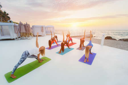 The group of women doing yoga at sunrise near the seaの写真素材