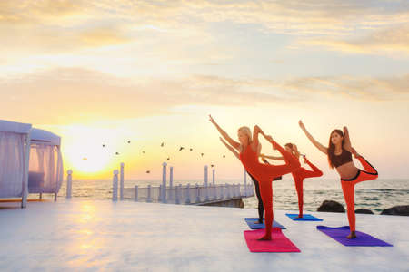 The group of women doing yoga at sunrise near the seaの写真素材