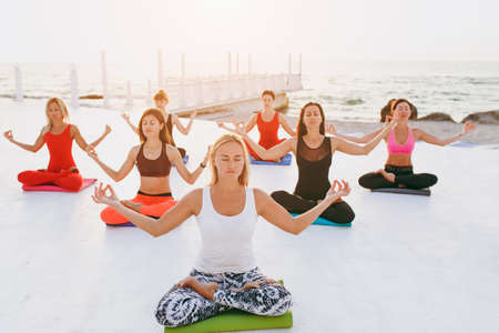 The group of women doing yoga at sunrise near the seaの写真素材