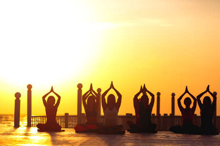 The group of women doing yoga at sunrise near the seaの写真素材