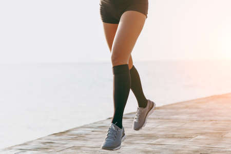 The girl's legs in black gaiters and gray sneakers, which runs in the morning at dawn near the seaの写真素材