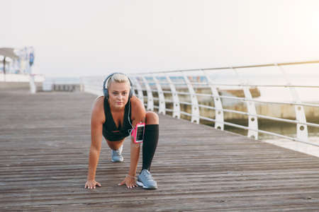 The young beautiful athletic girl with long blond hair in headphones listening to music and doing...