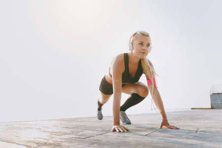 The young beautiful athletic girl with long blond hair in headphones and mobile phone on her hand...