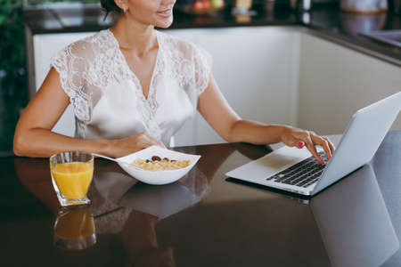 The portrait of beautiful young woman working with laptop while breakfast with cereals and milk....