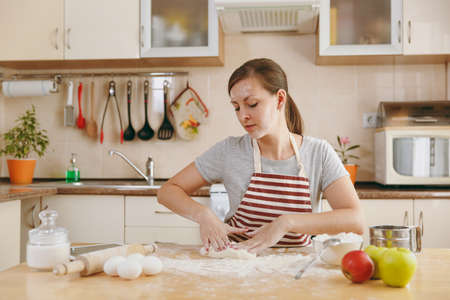 The young beautiful happy woman sitting at a table with flour, kneading dough and going to prepare a Christmas cakes in the kitchen. Cooking home. Prepare food.の写真素材