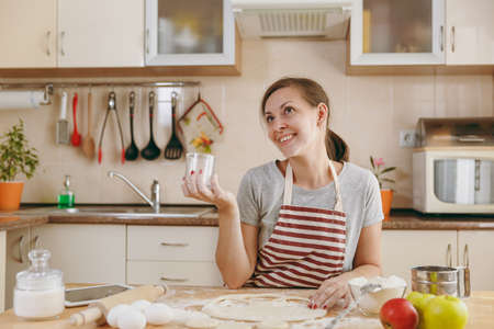 The young beautiful happy woman sitting at a table with flour and cut out a glass in a dough circles for dumplings in the kitchen. Cooking home. Prepare food.の写真素材