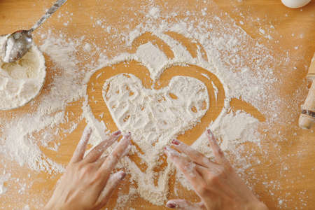 The hand drawn heart in flour on the kitchen table and other ingredients. Top view.