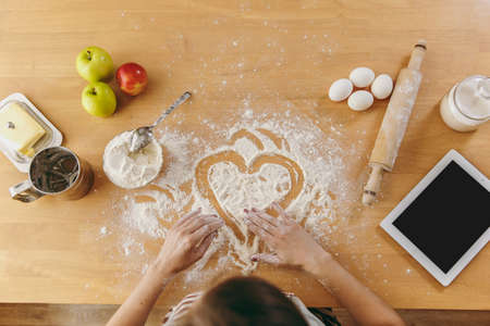 The hand drawn heart in flour on the kitchen table and other ingredients and tablet. Top view.の写真素材