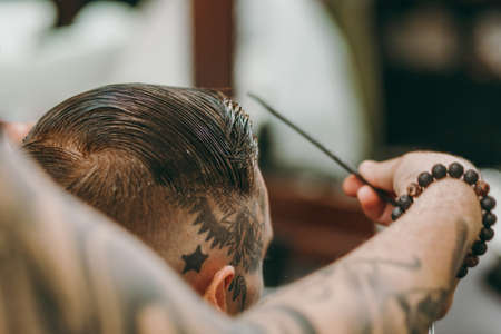 Close up shot of man getting trendy haircut at barber shop. The male hairstylist in tattoos serving client.の写真素材