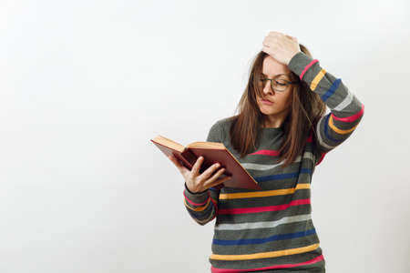 A beautiful European young brown-haired woman in glasses for sight dressed in casual dark grey longsleeve with colorful stripes, standing with book on a white background. Reading and studying conceptの写真素材