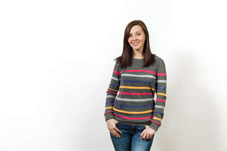 Pretty European happy brown-haired woman with healthy clean skin and charming smile, dressed in casual dark grey longsleeve with colorful stripes standing on a white background. Emotions conceptの写真素材