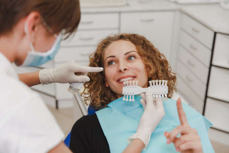 The dentist comparing patient's teeth shade with samples for bleaching treatmentの写真素材