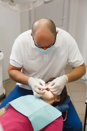 Close up process of preparing and installing dental ceramic crown. Male professional dentist helps to treat the teeth of woman patient in clinic light office with modern tools equipment. Open mouthの写真素材