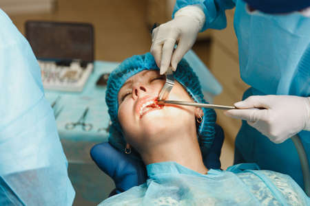 Close up process of male professional dentist surgeon performing operation install dental implant teeth of woman patient in clinic light office with modern tools equipment. Blood and pain on the faceの写真素材
