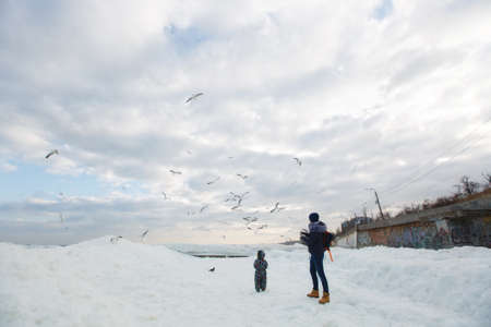 Woman play look at sea snow beach with little cute child baby boy in overalls with toy car, shovel. Mother, kid son fun on winter day. Family holiday 15 may love parents children concept. Back viewの写真素材