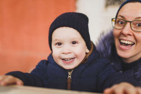 Young woman with little cute child baby boy look out from behind the handrail railing with columns. Mother, little kid son have fun. Parenthood, family day 15 of may, love, parents, children conceptの写真素材