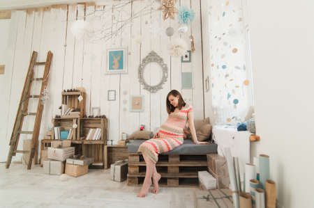 Happy pregnant young brunette woman in striped long dress with big belly in decor room, tummy, teddy bear. Pregnancy, parenthood, family, motherhood, parents, children, people and expectation conceptの写真素材