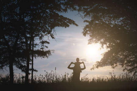 Silhouette of woman holding child baby boy on shoulders on nature, sunset trees background. Mother enjoying time with little kid son outdoors. Family day 15 of may, love, parents, children conceptの写真素材