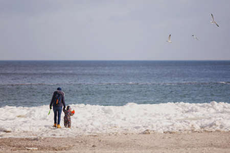 Woman play look at sea snow beach with little cute child baby boy in overalls with toy car, shovel. Mother, kid son fun on winter day. Family holiday 15 may love parents children concept. Back viewの写真素材
