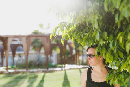 Beautiful caucasian happy brown-haired woman in sunglasses, black shirt rest in green nature outdoors. Summer sunny day in Egypt. Concept of tourism, vacation, recreationの写真素材