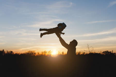 Silhouette of man high toss up little cute child baby boy on nature, sunset horizon background. Father throw up fun little kid son outdoors. Family day 15 of may, love, parents, children conceptの写真素材