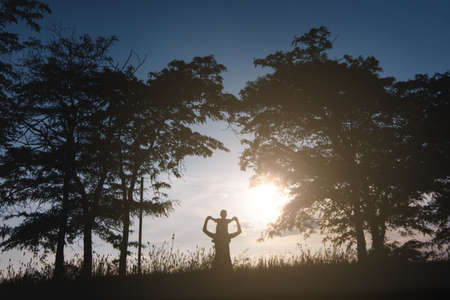 Silhouette of woman holding child baby boy on shoulders on nature, sunset trees background. Mother enjoying time with little kid son outdoors. Family day 15 of may, love, parents, children conceptの写真素材
