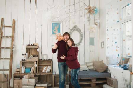 Happy pregnant young woman with big belly tummy, man in decor room. Couple with taddy bear. Wife, husband. Pregnancy, parenthood, family, motherhood, parents, children, people and expectation conceptの写真素材