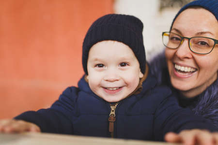 Young woman with little cute child baby boy look out from behind the handrail railing with columns. Mother, little kid son have fun. Parenthood, family day 15 of may, love, parents, children conceptの写真素材