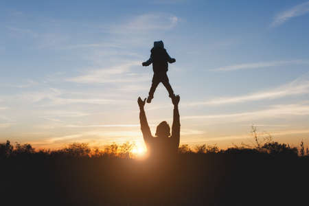 Silhouette of man high toss up little cute child baby boy on nature, sunset horizon background. Father throw up fun little kid son outdoors. Family day 15 of may, love, parents, children conceptの写真素材