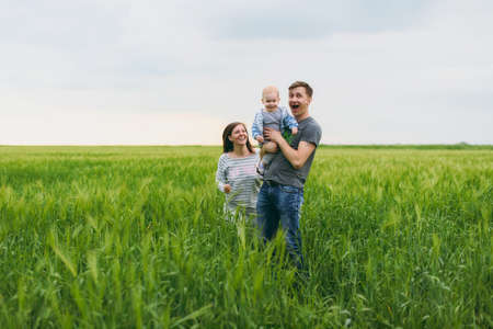 Joyful man, woman walk on green field background, rest, have fun, play, stand with little cute child baby boy. Mother, father, little kid son. Family day 15 of may, love, parents, children conceptの写真素材